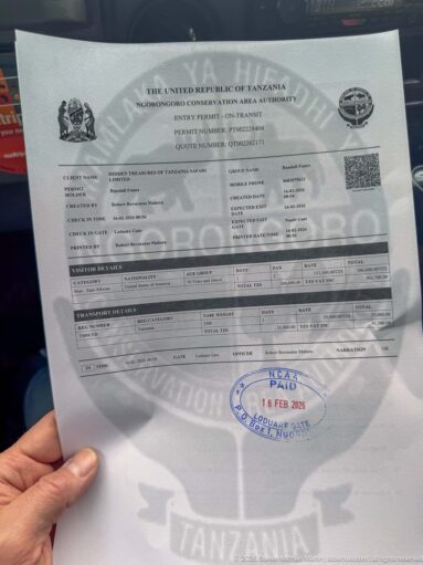 Official Ngorongoro Conservation Area Authority permit held by hand, showing visitor fields, QR code, and blue dated entry stamp.
