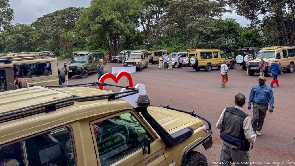 Safari Land Cruisers parked around a paved lot with visitors and guides walking between vehicles near Lodoare Gate.