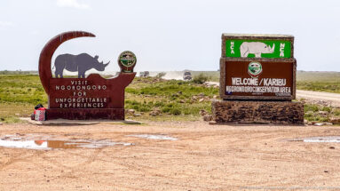 Two Ngorongoro Conservation Area welcome monuments beside a dirt road, including rhinoceros graphics and bilingual welcome lettering.