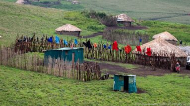 Fenced highland settlement with round thatched huts, small structures, and brightly colored clothing hanging along stick enclosures.