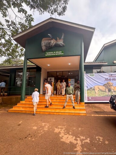 Visitors climbing orange steps into a green Lodoare Gate building beneath a large wildlife emblem.