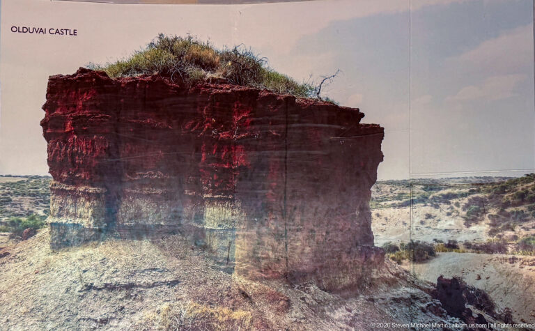 Steep eroded outcrop with dark red upper beds over paler gray and tan sedimentary layers.