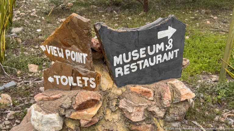 Hand-painted stone sign pointing toward the viewpoint, toilets, museum, and restaurant at Olduvai Gorge.