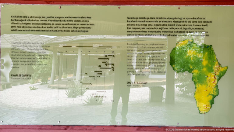 Transparent interpretive panel with a colored map of Africa, quotations, and the museum courtyard visible behind.