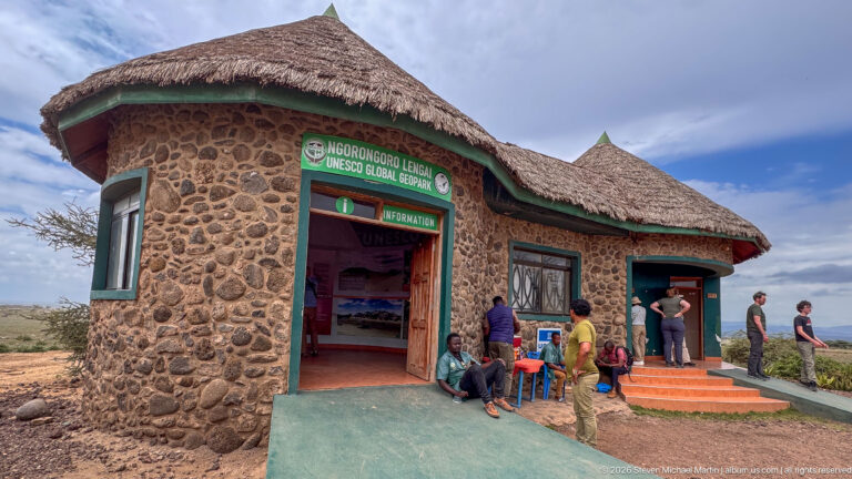 Angled view of the stone-and-thatch UNESCO Global Geopark information office with visitors at open windows.