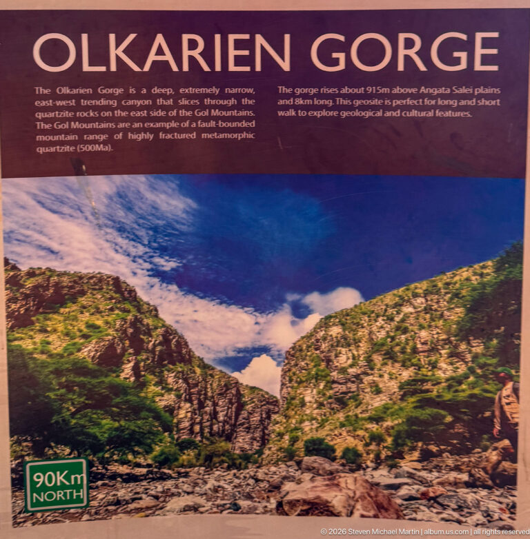 Olkarien Gorge interpretive panel with a narrow rocky ravine between steep green slopes.