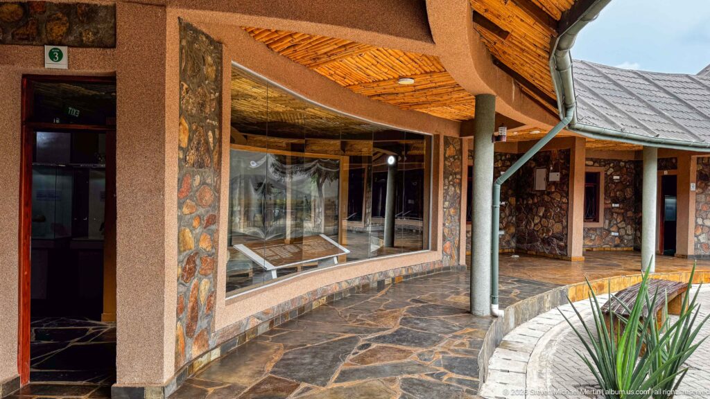 Curved museum gallery with stone walls, glass display windows, columns, and a broad shaded roof.