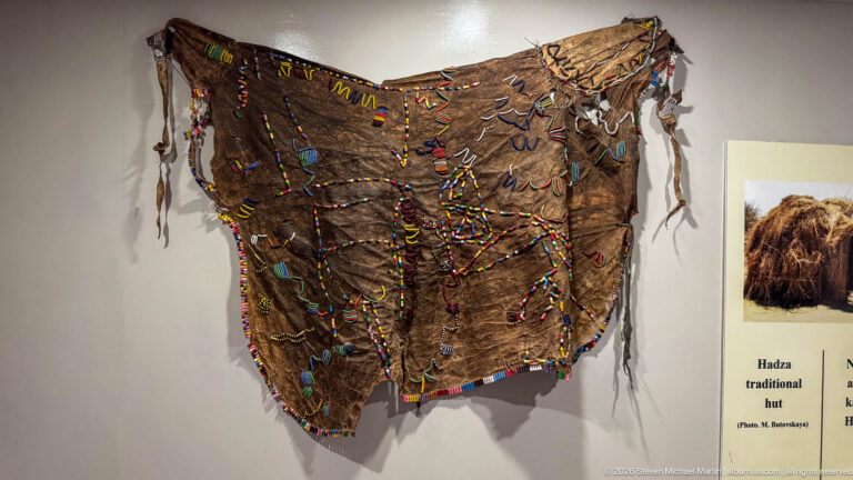 Large brown hide garment covered with multicolored beadwork, stitched decoration, and hanging leather ties.