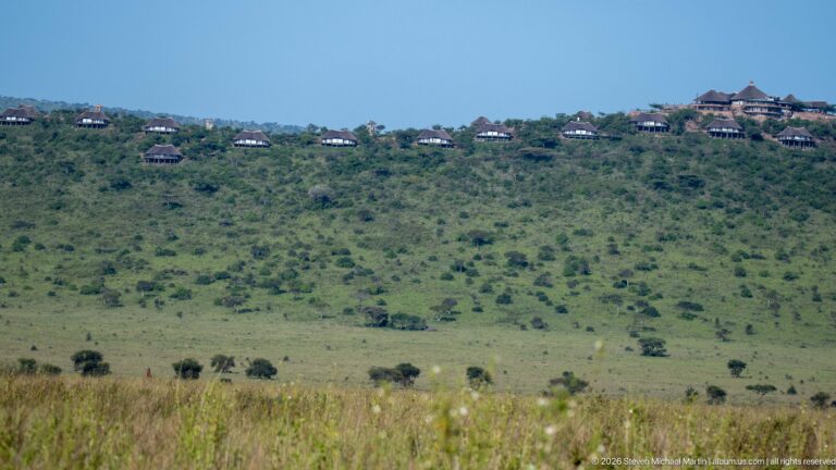 Distant line of small lodge buildings along a green ridge, with a larger complex at the far right.