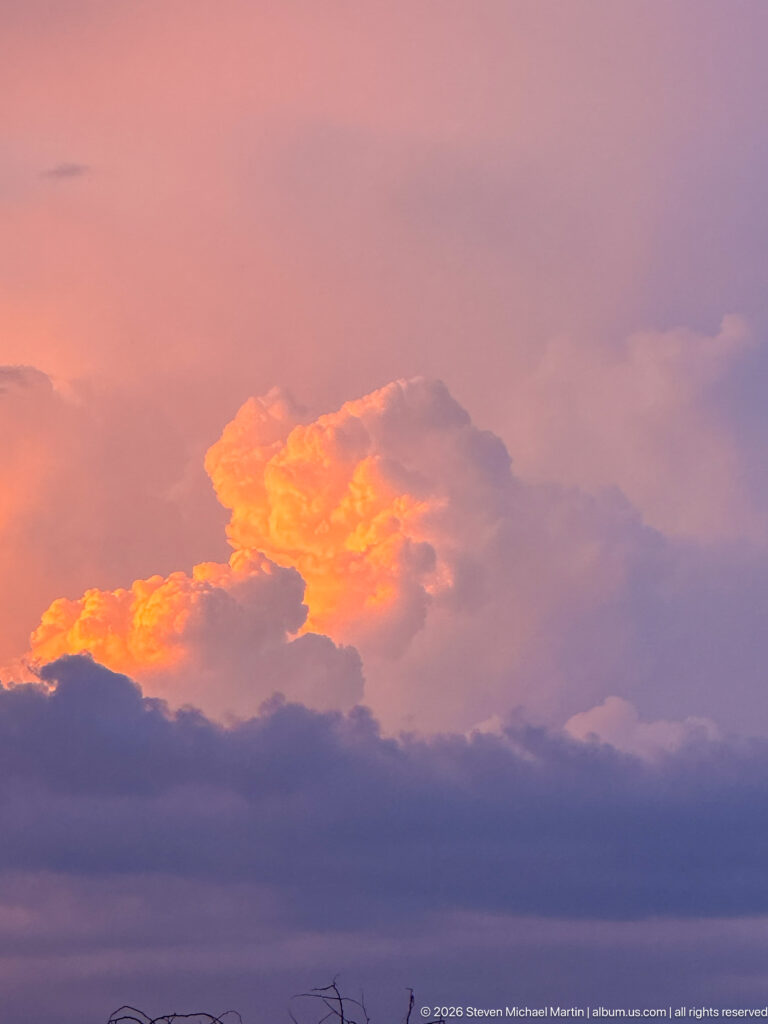 Orange-lit towering clouds rising through violet and blue-gray layers at dusk over the Serengeti.