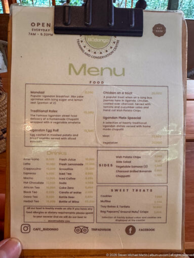 Printed café menu on a clipboard listing breakfast, traditional dishes, snacks, sides, and drinks.