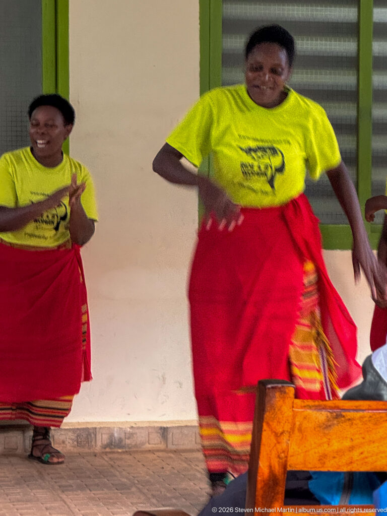 Woman in a yellow shirt and red wrap skirt dances in the foreground while another performer claps behind her.