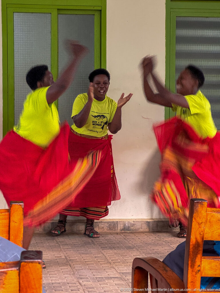 Three women in yellow tops and red wrap skirts dance energetically on a veranda, their skirts and arms blurred in motion.
