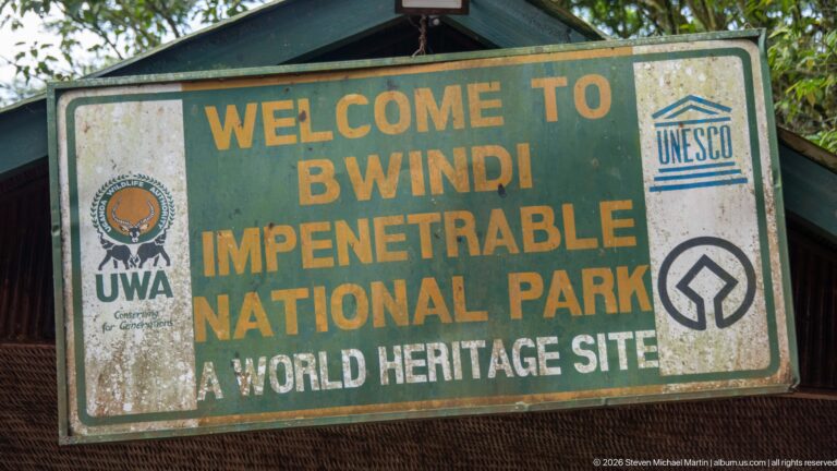 Weathered green sign reading Welcome to Bwindi Impenetrable National Park, A World Heritage Site, with UWA and UNESCO emblems.