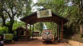 Safari vehicle driving beneath the covered Bwindi Impenetrable National Park entrance, with checkpoint booth and warning sign beside the road.