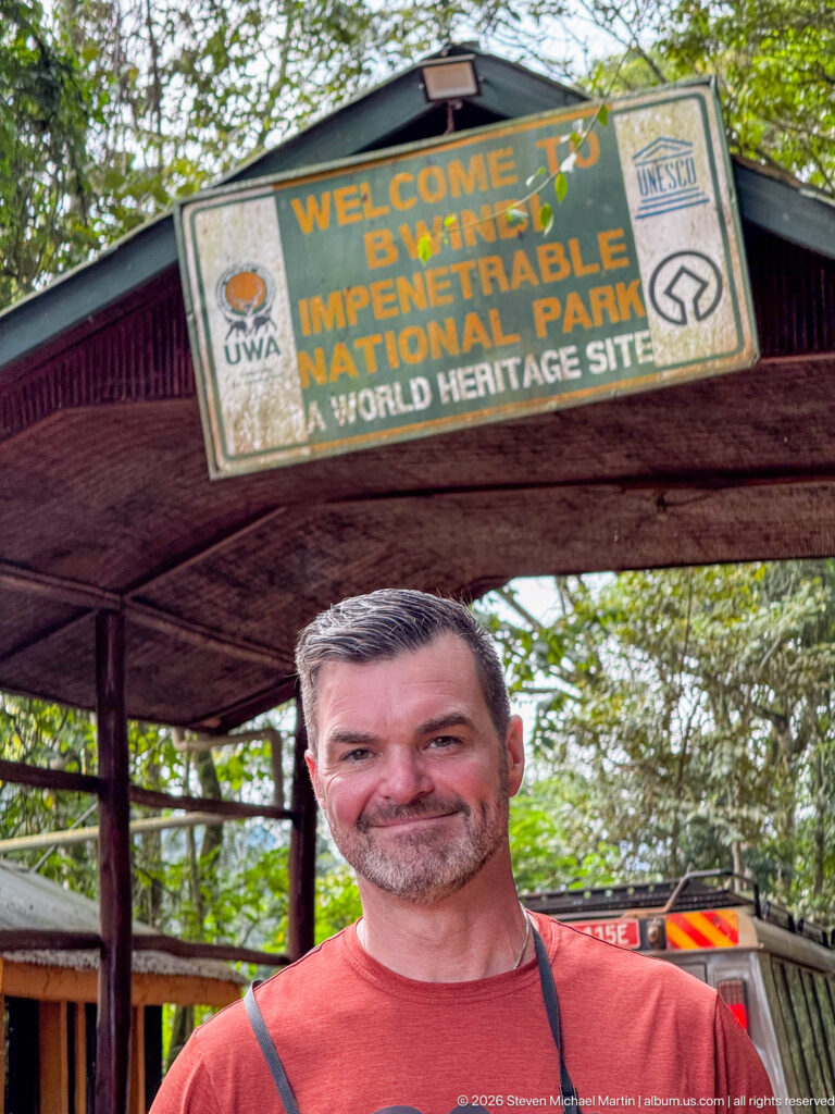 Close portrait of a man beneath the Bwindi Impenetrable National Park gateway sign marked as a World Heritage Site.