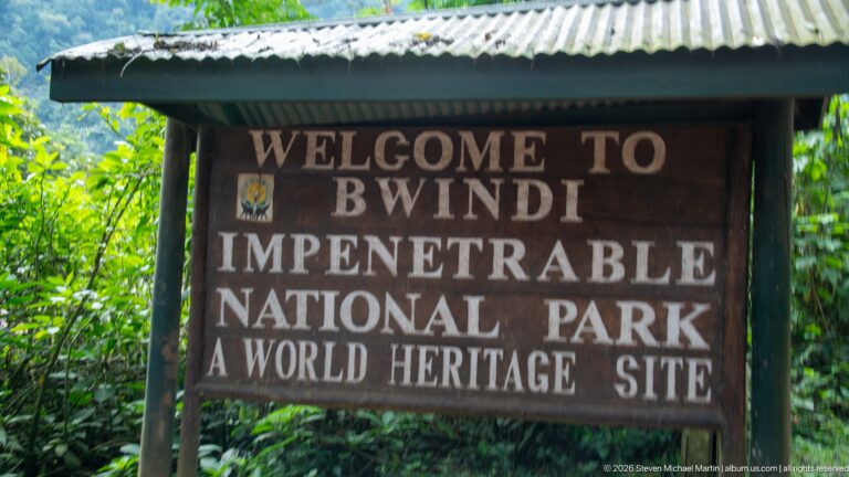 Close view of the wooden Welcome to Bwindi Impenetrable National Park, A World Heritage Site sign surrounded by green vegetation.