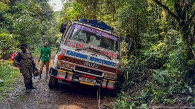 Decorated Isuzu truck angled on a narrow muddy forest road with people standing nearby.