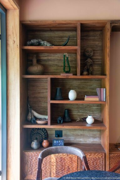 Wooden built-in shelves displaying bowls, beads, books, carved objects and woven baskets in a lodge interior.