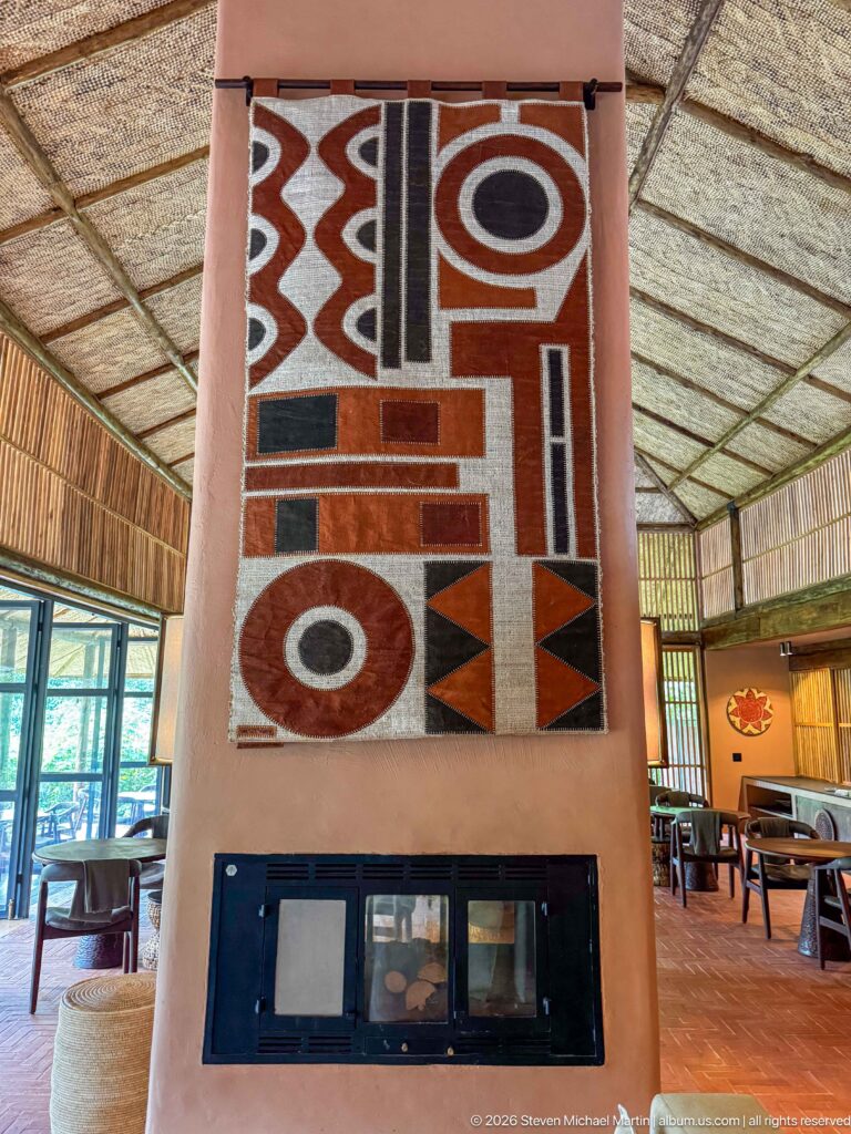 Bold geometric textile in red, black, cream and brown mounted above a dark glazed lodge fireplace.