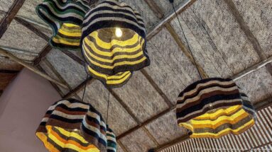 Cluster of striped woven pendant shades in black, cream, yellow, green and rust hanging beneath a textured ceiling.