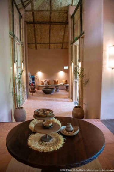 Round wooden table set with woven circular mats and ceramic pieces, with a low seating area visible beyond.
