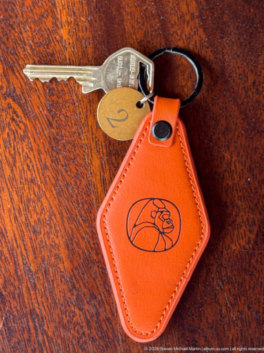 Orange leather key fob with embossed animal motif, metal key and round tag marked 2 on a wooden surface.