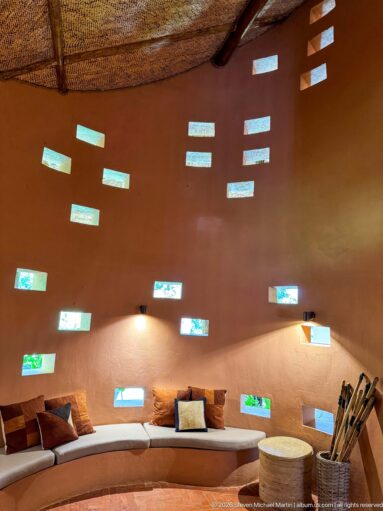 Curved ochre lounge wall dotted with small rectangular windows above a long built-in cushioned bench.
