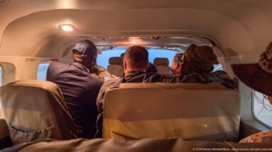 Rear-to-front view inside a small aircraft cabin with passengers seated closely together ahead.