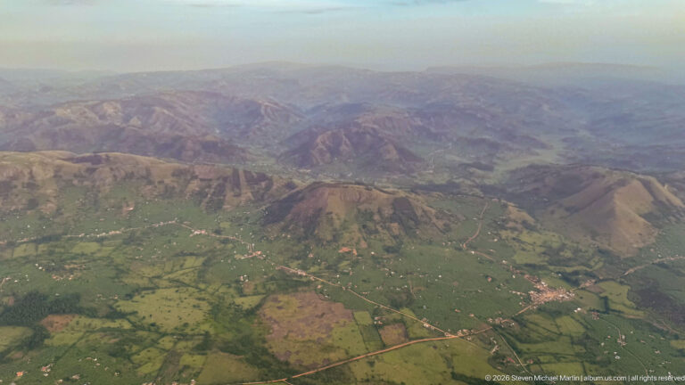 Patchwork farmland and settlements spread across valleys below rugged brown and green ridges.