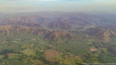 Patchwork farmland and settlements spread across valleys below rugged brown and green ridges.