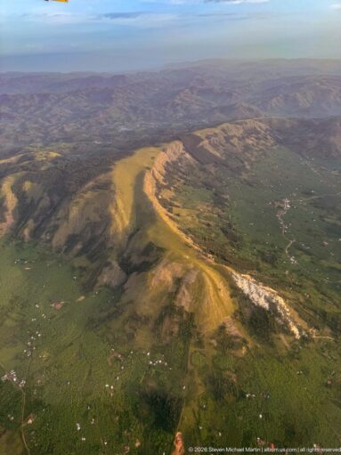 Long sunlit ridge with exposed pale slopes rising above green farmland and scattered settlements.
