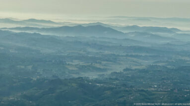 Layered blue-gray mountain ridges with cultivated slopes and scattered settlement in western Uganda.