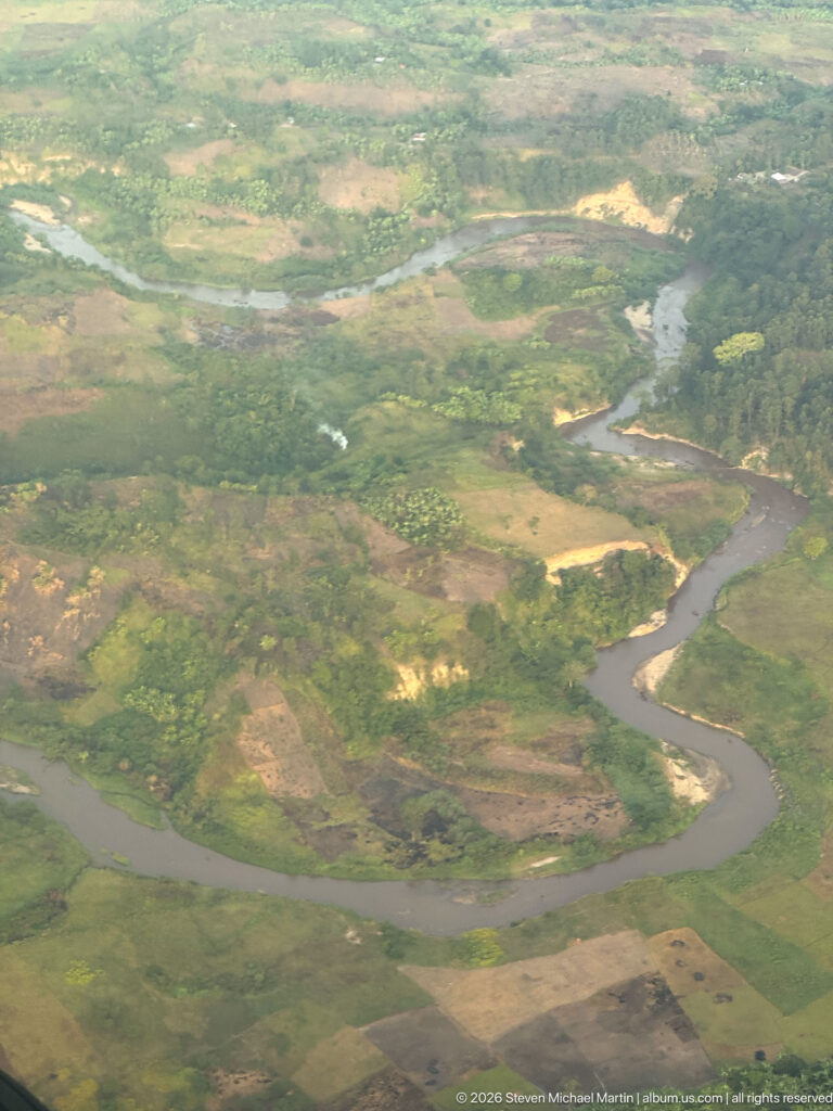 Broad brown river making a horseshoe bend through green floodplain and cultivated land.