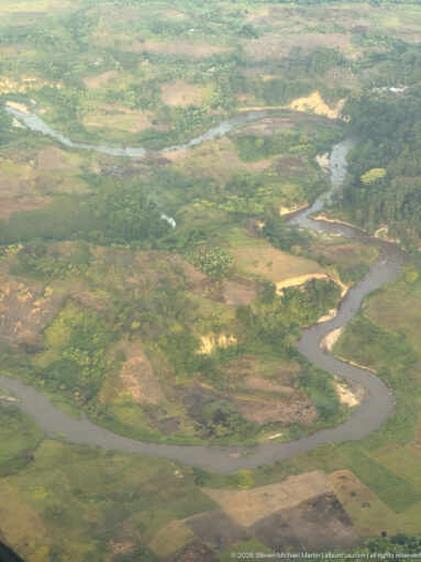 Broad brown river making a horseshoe bend through green floodplain and cultivated land.