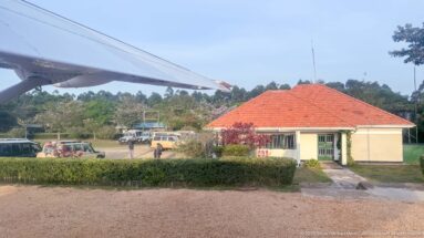 Red-roofed Kihihi terminal and parked vehicles seen beneath the wing of a departing light aircraft.