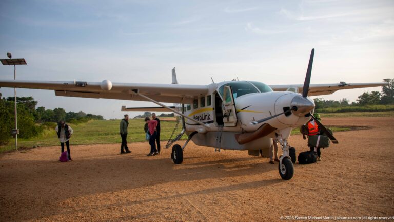 Aerolink Uganda high-wing single-engine turboprop on the Kihihi apron with passengers and staff beside the open door.