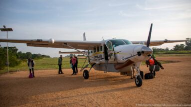 Aerolink Uganda high-wing single-engine turboprop on the Kihihi apron with passengers and staff beside the open door.