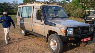 Long-wheelbase safari vehicle with raised roof, snorkel, and brush guard parked on the dirt apron at Kihihi.