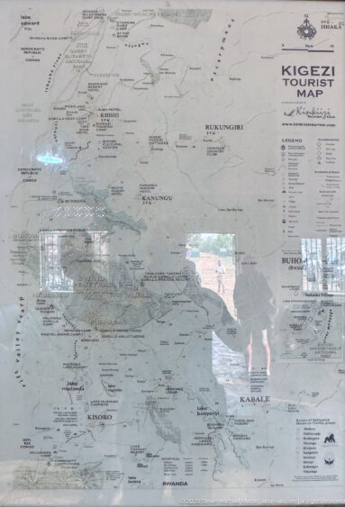 Wall-mounted Kigezi Tourist Map with roads, towns, parks, and lakes visible beneath reflective glazing.