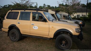 Beige Toyota four-wheel-drive safari vehicle with roof rack and off-road tires parked beside similar vehicles.