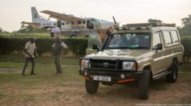 Toyota four-wheel-drive safari vehicle parked in front of an AeroLink turboprop aircraft as two people stand nearby.