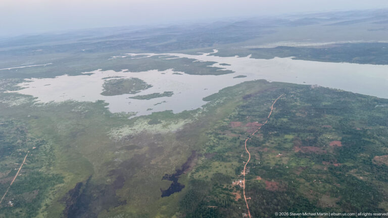 Branching shallow water, marshy islands, low peninsulas, and a reddish road across settled green land.