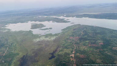 Branching shallow water, marshy islands, low peninsulas, and a reddish road across settled green land.
