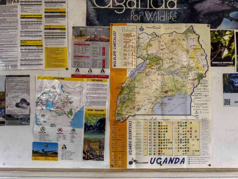 Information board covered with a large Uganda map, wildlife photographs, notices, and travel information.