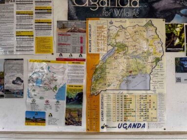 Information board covered with a large Uganda map, wildlife photographs, notices, and travel information.