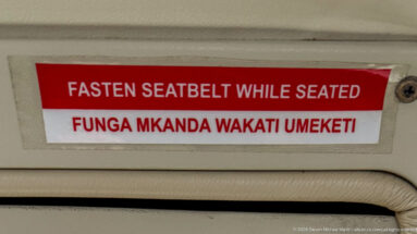 Red-and-white aircraft placard reading Fasten Seatbelt While Seated with the same instruction in Swahili below.