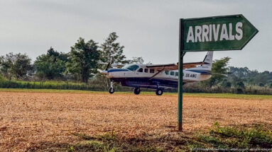Green ARRIVALS arrow sign beside a gravel airstrip with a small high-wing aircraft in the background.