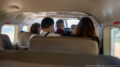 Rear-to-front view inside a small aircraft cabin with several seated passengers facing the cockpit.