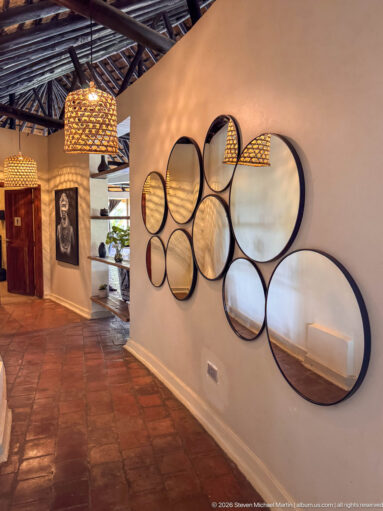 Cluster of black-rimmed circular mirrors of different sizes on a pale lodge wall beside woven pendant lights.